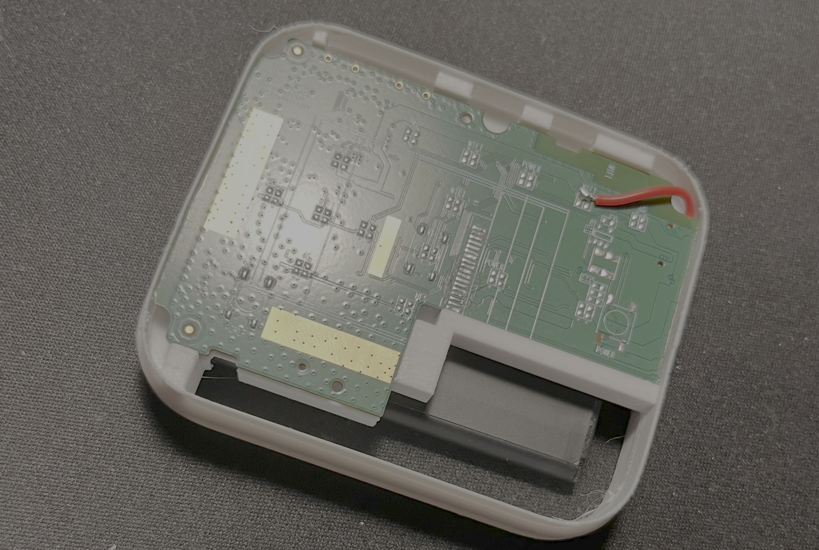 The cut PCB inside a test enclosure with the battery below and the patch VBAT wire